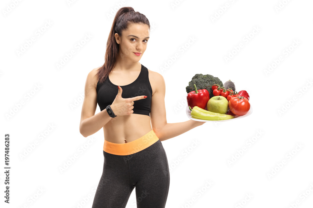 Fitness woman holding a plate of vegetables and fruit and pointing Fitness woman holding a plate of vegetables and fruit and pointing