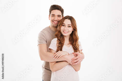 Young lovely couple boyfriend and girlfriend posing together with broad smile while man hugging woman happily, over white background