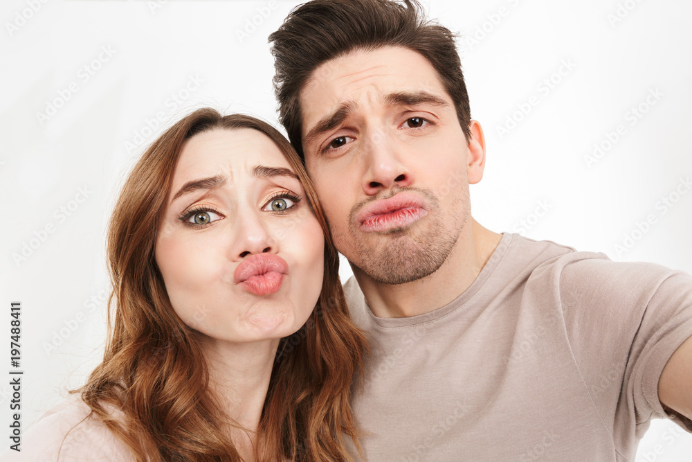 Closeup picture of amusing couple in relationship looking on camera and blowing air kiss while photographing themselves, isolated over white background Closeup picture of amusing couple in relationship looking on camera and blowing air kiss while photographing themselves, isolated over white background