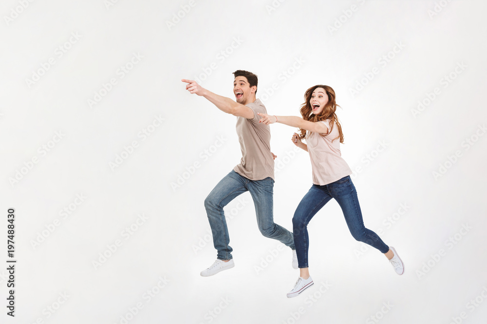 Full-length picture of delighted couple man and woman in casual t-shirt and jeans running and pointing fingers on copyspace with smile, isolated over white background Full-length picture of delighted couple man and woman in casual t-shirt and jeans running and pointing fingers on copyspace with smile, isolated over white background