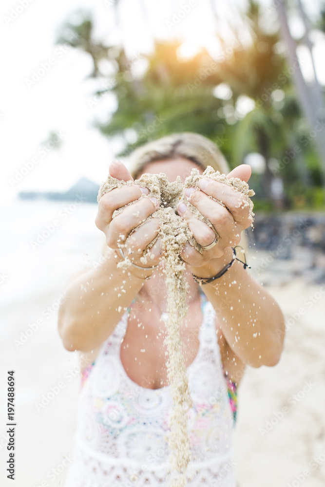 Fototapeta premium young pretty woman lets sand trickle from her hands an a beautiful beach in thailand