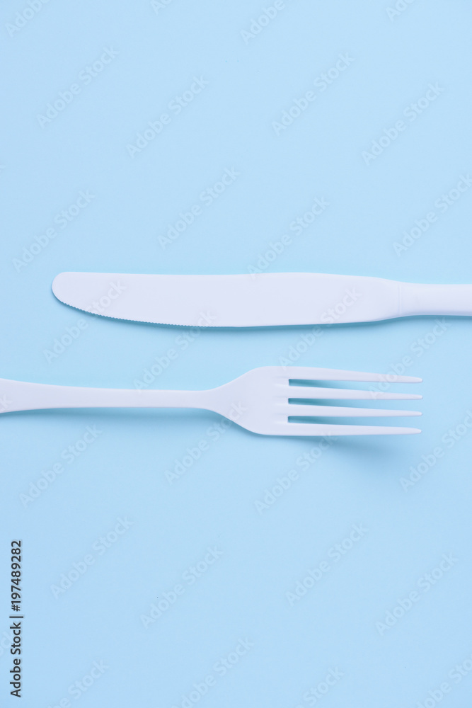Clean new white knife and fork creative flat lay on trendy soft blue paper background Clean new white knife and fork creative flat lay on trendy soft blue paper background