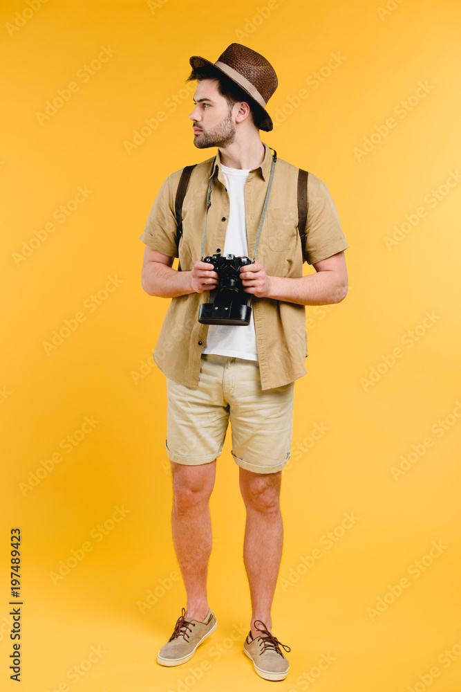young male traveler in shorts holding camera and looking away isolated on yellow young male traveler in shorts holding camera and looking away isolated on yellow