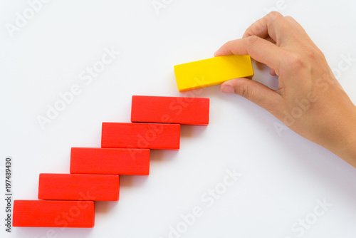 Concept of building success foundation. Women hand put yellow wooden block on red wooden blocks in the shape of a staircase