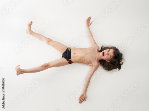 Long-haired little boy in a swimsuit lying on his back, isolated on a light