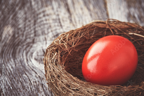 Red Easter egg in nest on old wooden background. Copy space, toned, soft focus