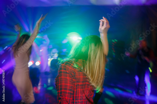 The girl is dancing with her back on the dance floor. Multicolored disco lights