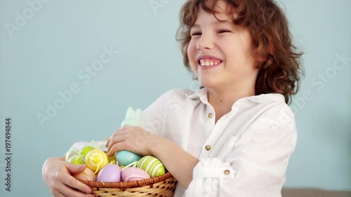 Cheerful schoolboy with a basket of Easter eggs. Curly-haired boy laughs fun photo