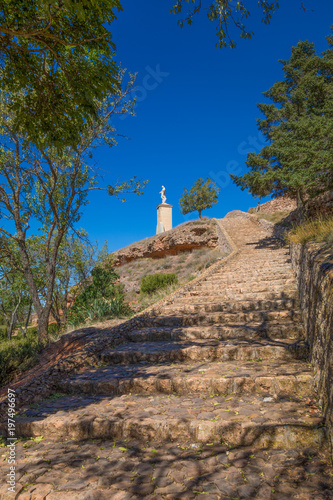 stone stairs climbing to the top of mountain in nature between trees and blue sky, with a statue of Jesus Christ in Ayllon village, Segovia, Spain, Europe 