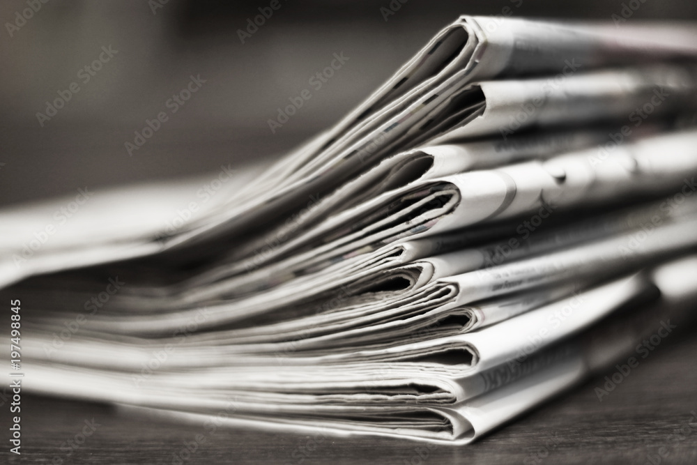 Folded newspapers on the desk. Pile of daily papers with business news, side view, selective focus Folded newspapers on the desk. Pile of daily papers with business news, side view, selective focus