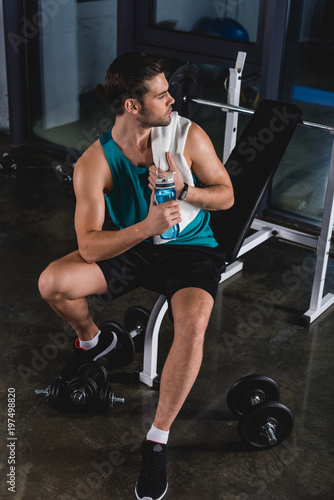 tired sportsman resting with towel and sport bottle in gym