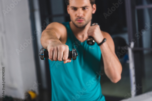 selective focus of sportsman exercising with dumbbells in sports center