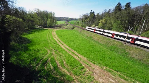 Scenic aerial shot of a commuter train passing through the countryside. Cinematic shot - drone rising when the train enters the frame