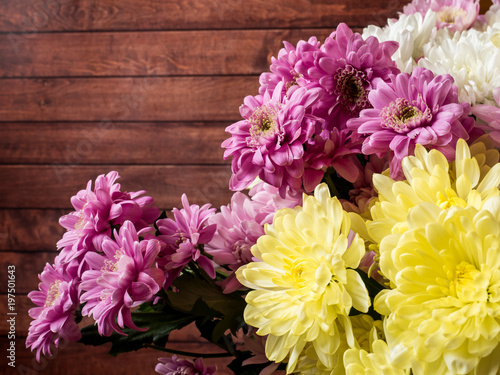 Bouquet of multicolored chrysanthemums on brown wooden background Place for text