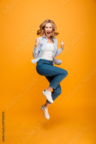 Fototapeta Naklejka Na Ścianę i Meble -  Full length picture of content ecstatic adult girl expressing delight and clenching fists, isolated over yellow background