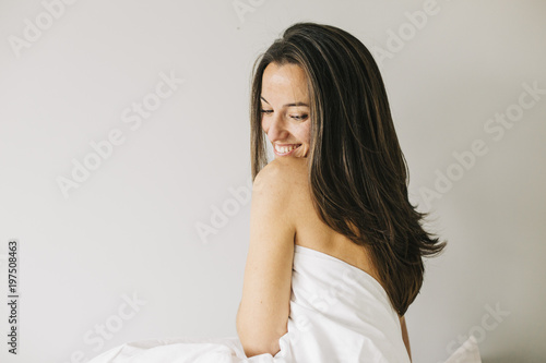 young beautiful woman sitting on bed, resting and smiling. Lifestyle at home. Indoors. Portrait