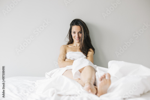 young beautiful woman sitting on bed, resting and smiling. Lifestyle at home. Indoors. Portrait