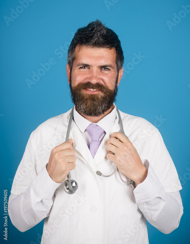 Treatment, medicine, healthcare and medical concept - smiles physician with stethoscope in white medical gown. Closeup portrait bearded, handsome and confident doctor with stethoscope.