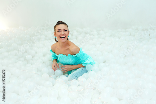 Happy beautiful woman lays surrounded by white plastic balls in the dry pool for adult. Copy splace. photo