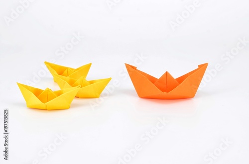 Leadership concept with a orange paper ship leading among yellow ships.