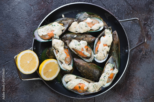 Metal pan with green mussels baked in cheese sauce, view from above on a weathered asphalt background, horizontal shot