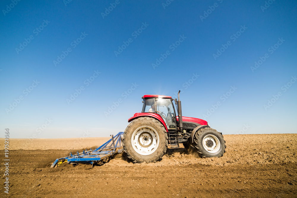Obraz premium Tractor cultivating field at spring