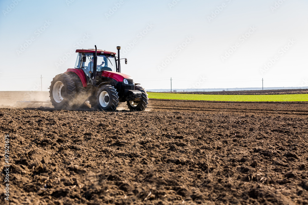Obraz premium Tractor cultivating field at spring