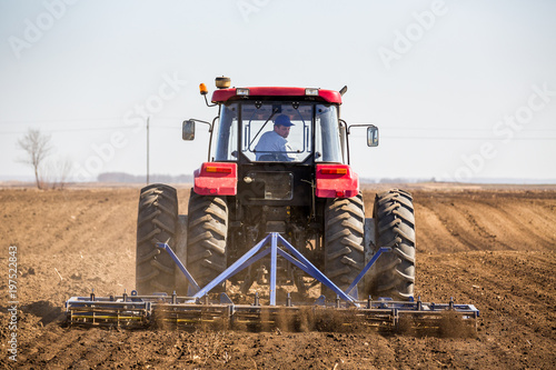 Fotografia Tractor cultivating field at spring