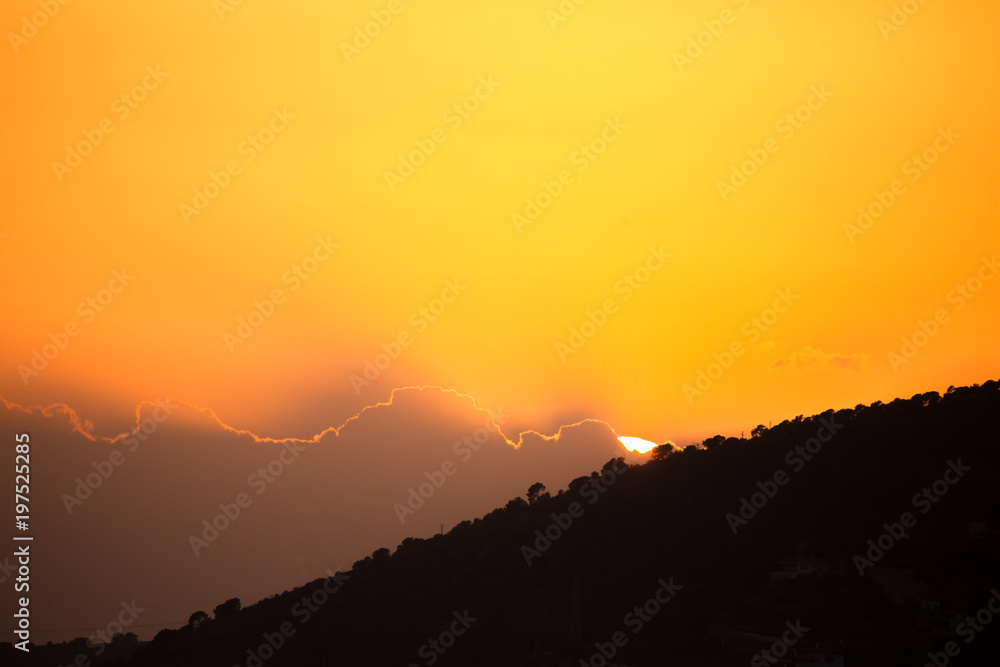 Sun hiding among clouds and mountains under a yellow sky Sun hiding among clouds and mountains under a yellow sky