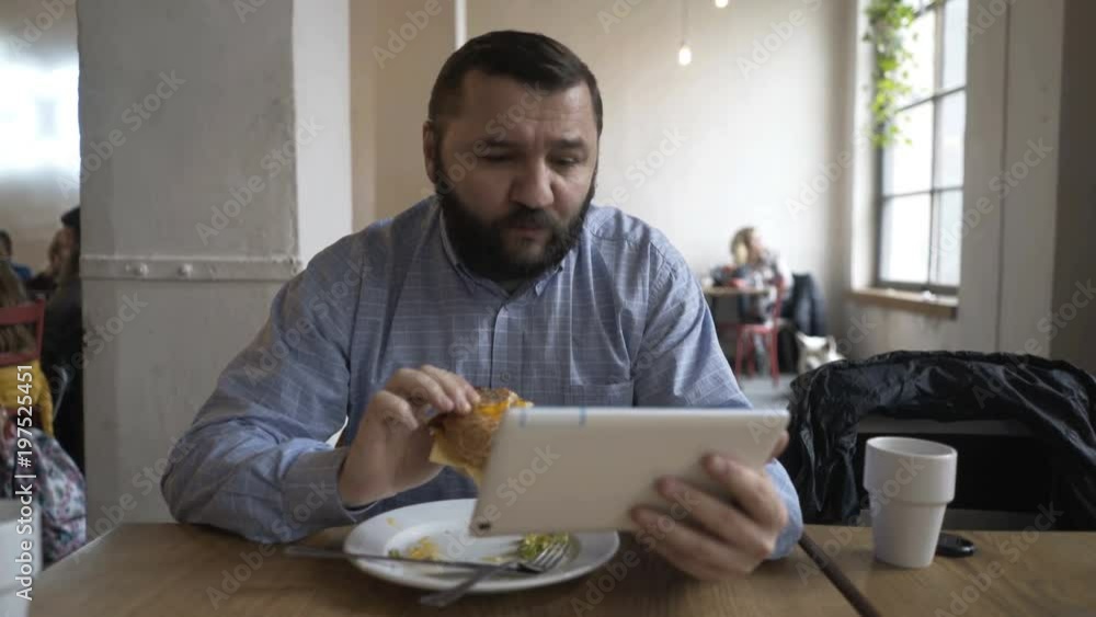 Man watching movie on tablet eating hamburger in cafe
Man watching movie on tablet eating hamburger in cafe