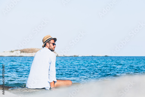 Young man relaxing on the beach  sitting on a rock near the sea