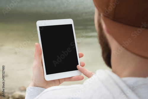 фотографія Close-up of a horde in a brown cap in the open air holds a white tablet pc in his hands