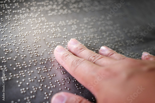The blind fingers touching the Braille letters on the metal plate 