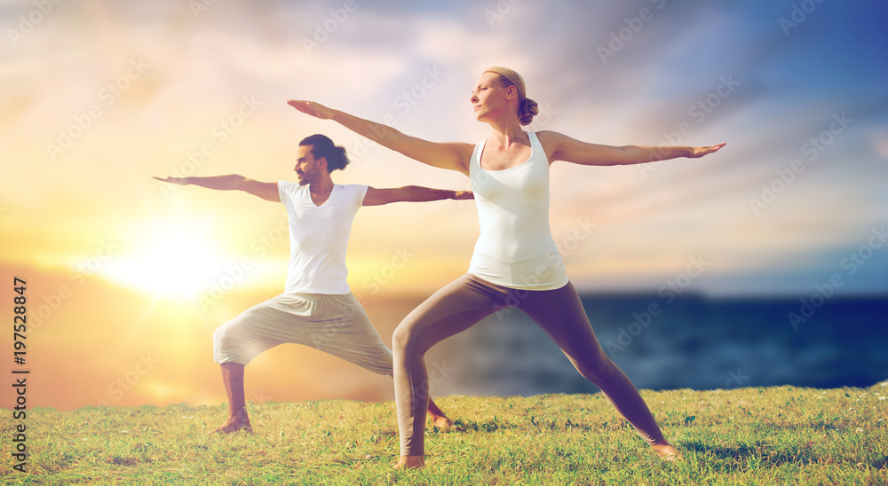 fitness and people concept - couple making yoga warrior pose outdoors over sea background fitness and people concept - couple making yoga warrior pose outdoors over sea background