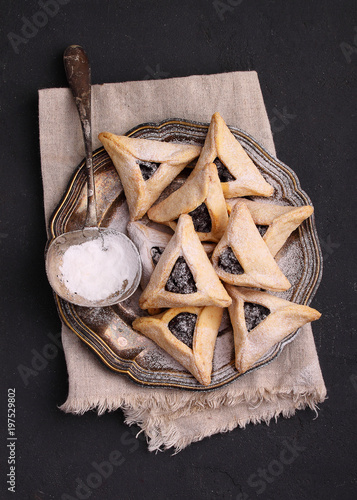 Hamantaschen cookies with poppy seed and risins and icing sugar on a plate, cooked for Jewish festival of Purim.