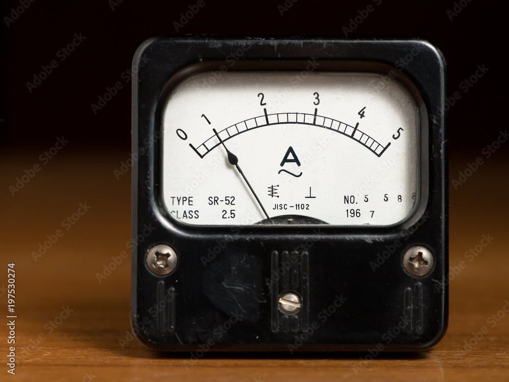 An old black analog ampere meter on a wooden table An old black analog ampere meter on a wooden table