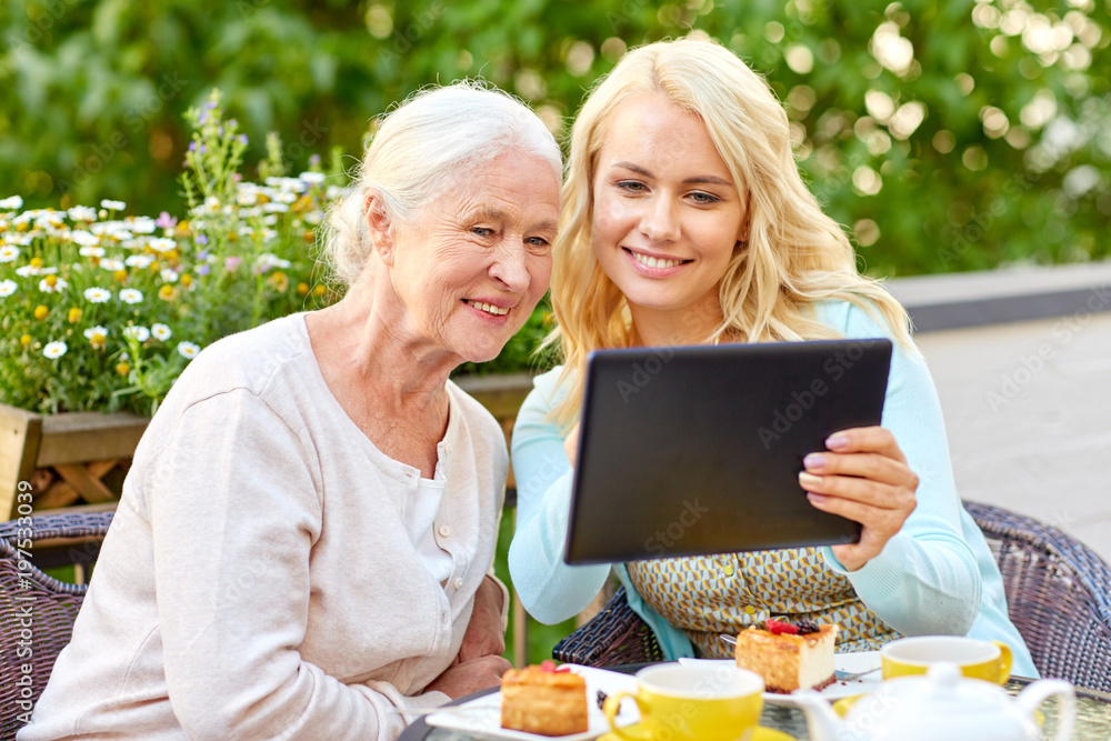 family, technology and people concept - happy smiling young daughter with tablet pc computer and senior mother at cafe or restaurant terrace family, technology and people concept - happy smiling young daughter with tablet pc computer and senior mother at cafe or restaurant terrace