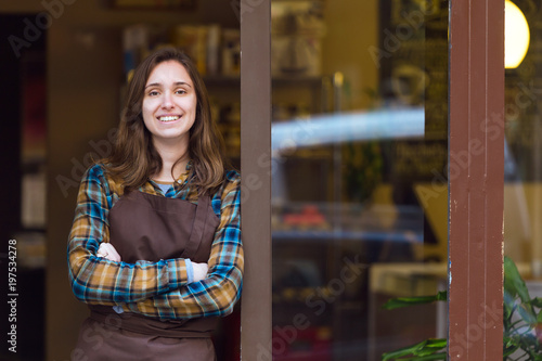 Foto Beautiful young saleswoman looking at camera and leaning against the door frame of an organic store