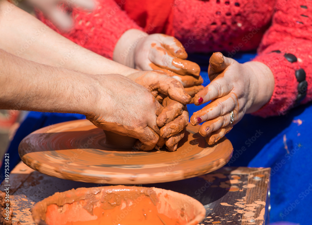 The hands of a potter work with clay on a potter's wheel