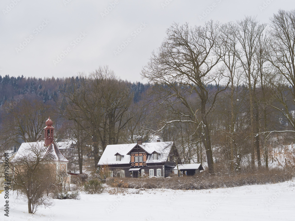 winter view on village travnik with chapel, timbered cottage nad trees, snow covered rural landscape with in luzicke hory mountain