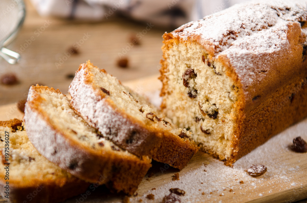 A homemade cake with raisins and powdered sugar is cut on wooden table. White napkin