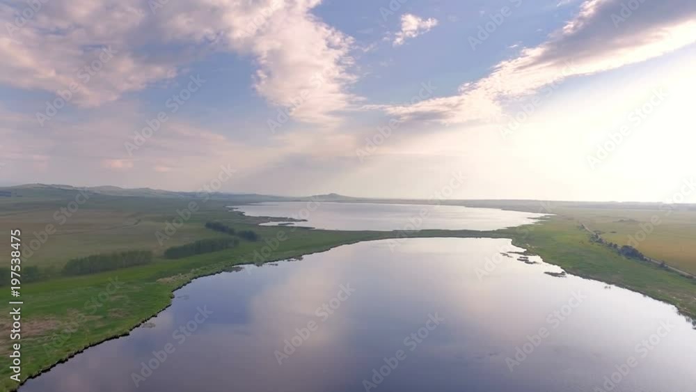 AERIAL: Beautiful landscape of a green valley with endless lakes. Reflections of clouds on the water, a mountain chain and hills in the background. AERIAL: Beautiful landscape of a green valley with endless lakes. Reflections of clouds on the water, a mountain chain and hills in the background.