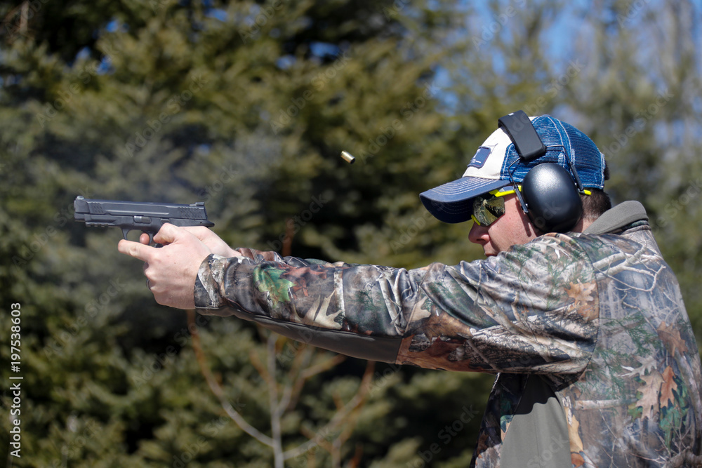 Fototapeta premium Man shooting a pistol; ejected cartridge case in the air.