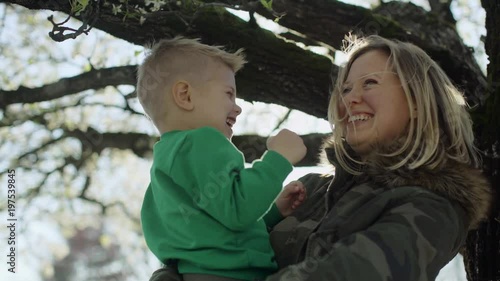 Portrait of happy young woman holding her baby son under tree at backyard 4k