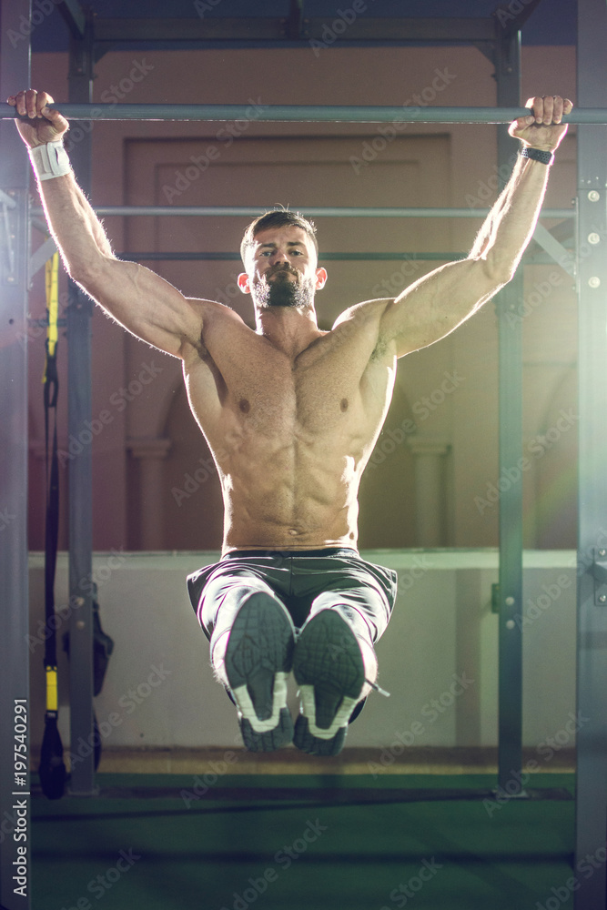 Handsome shirtless man doing pull ups in the L-sit position on horizontal  bar outdoors at night. Calisthenics training. Stock Photo