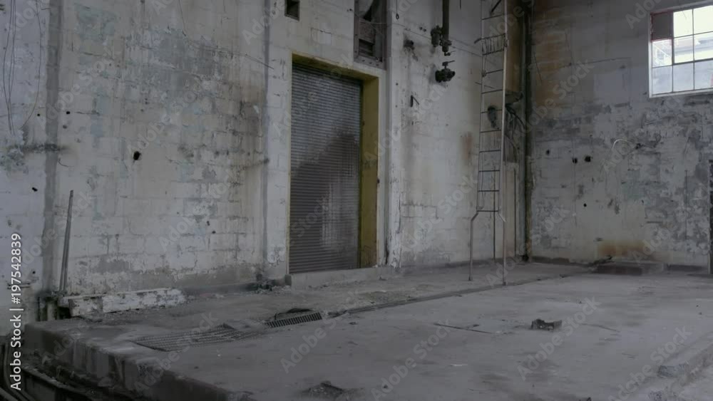A tilt shot of metal catwalk and broken air vents down to a garage door and ladder in an abandoned factory. A tilt shot of metal catwalk and broken air vents down to a garage door and ladder in an abandoned factory.