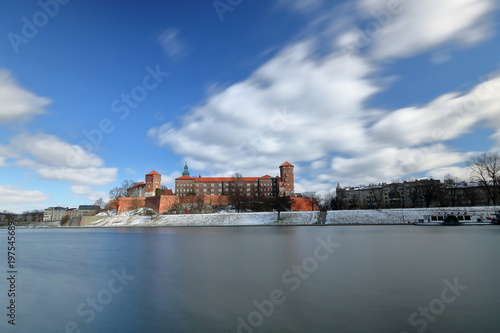 Symbol Krakowa, Polska, zamek na Wawelu, z przeciwnego brzegu rzeki Wisły, słoneczny, dzień, resztki śniegu, błękitne niebo z płynącymi, rozmytymi białymi obłokami, długie naświetlanie