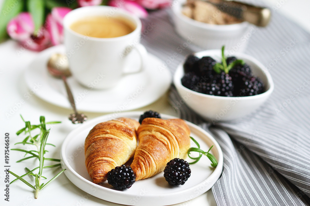 Morning breakfast with cup of coffee, croissants, fresh berries and pink flowers tulips on white tray, brown sugar