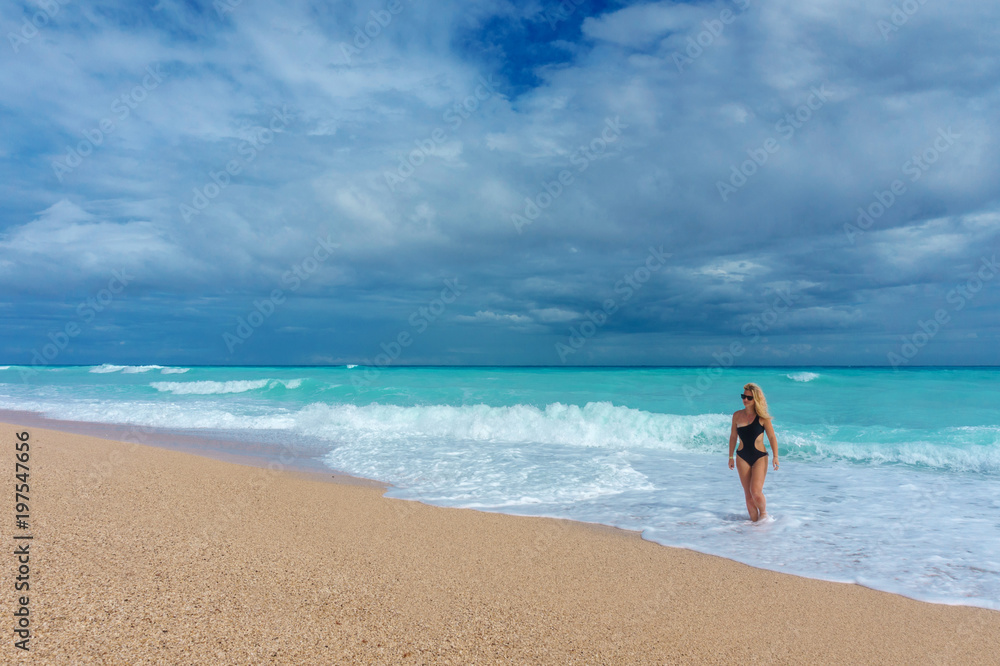 beautiful blonde girl in a black swimwear walking on an empty Caribbean beach beautiful blonde girl in a black swimwear walking on an empty Caribbean beach