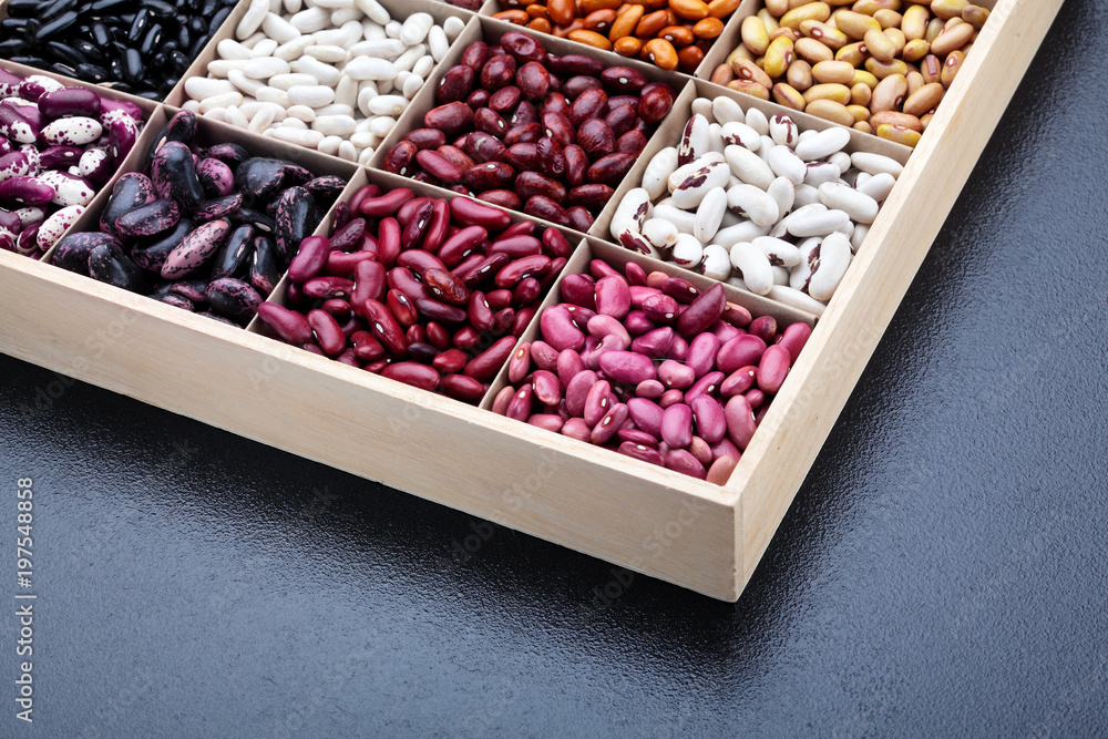 Different types of legumes beans. In wooden box.Varieties of beans.Top view.Closeup.Texture.Copy space.On dark stone background